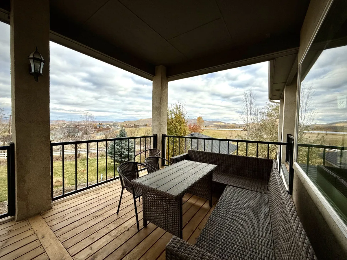 This image depicts a serene outdoor seating area with a table and chairs, all oriented toward an expansive, picturesque landscape. The horizon stretches into rolling hills or foothills, and the seating arrangement suggests a comfortable spot for both dining and lounging outdoors.