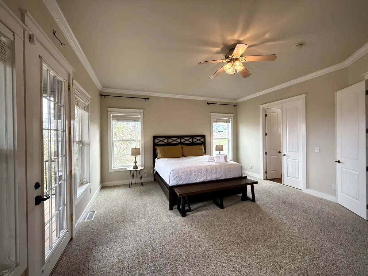 A tranquil bedroom featuring a neatly made bed with soft linens, nightstands with lamps on either side, and a bench at the foot of the bed. Soft, natural light filters through the windows, creating a serene, restful environment.