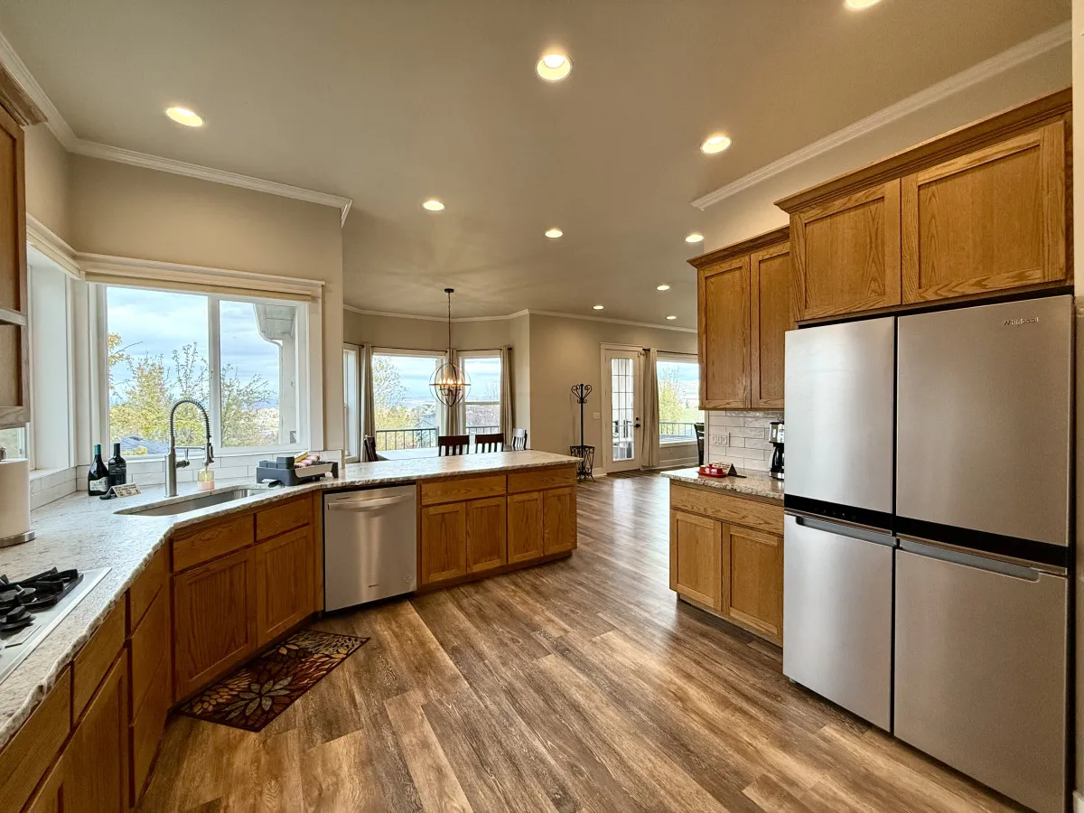 Here, a modern kitchen with a central island, stainless steel appliances, wood cabinetry, and expansive windows is depicted. The kitchen is both functional and stylish, suited to hosting and gourmet cooking, with plenty of space for guests to mingle while enjoying foothill or golf course views beyond the glass.