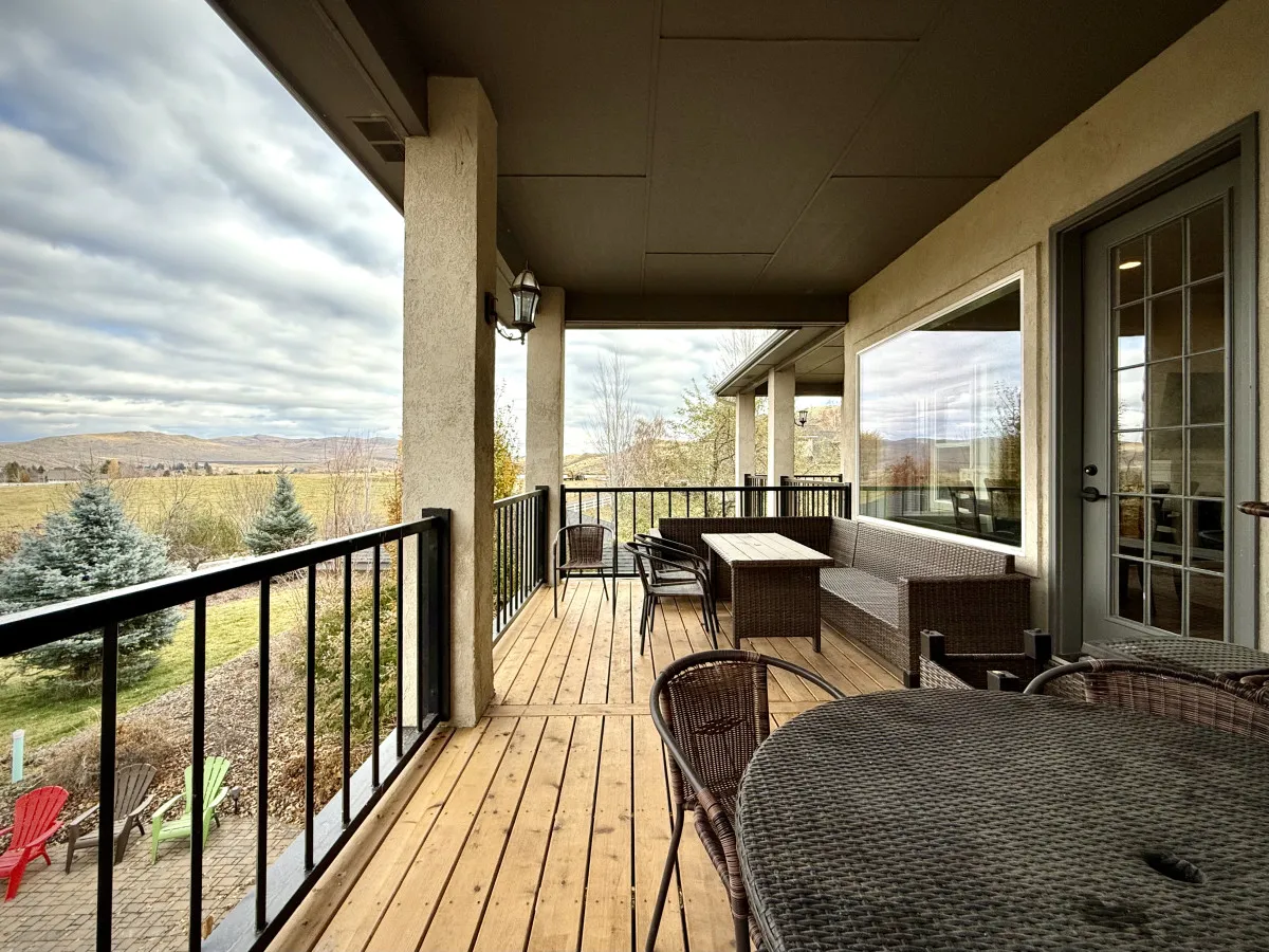 A wooden deck furnished with wicker outdoor seating and a small table, all under open sky with mountain and scenic views beyond the railing. The setup is inviting for both relaxation and socializing, suggesting a space that is both elegant and comfortable.