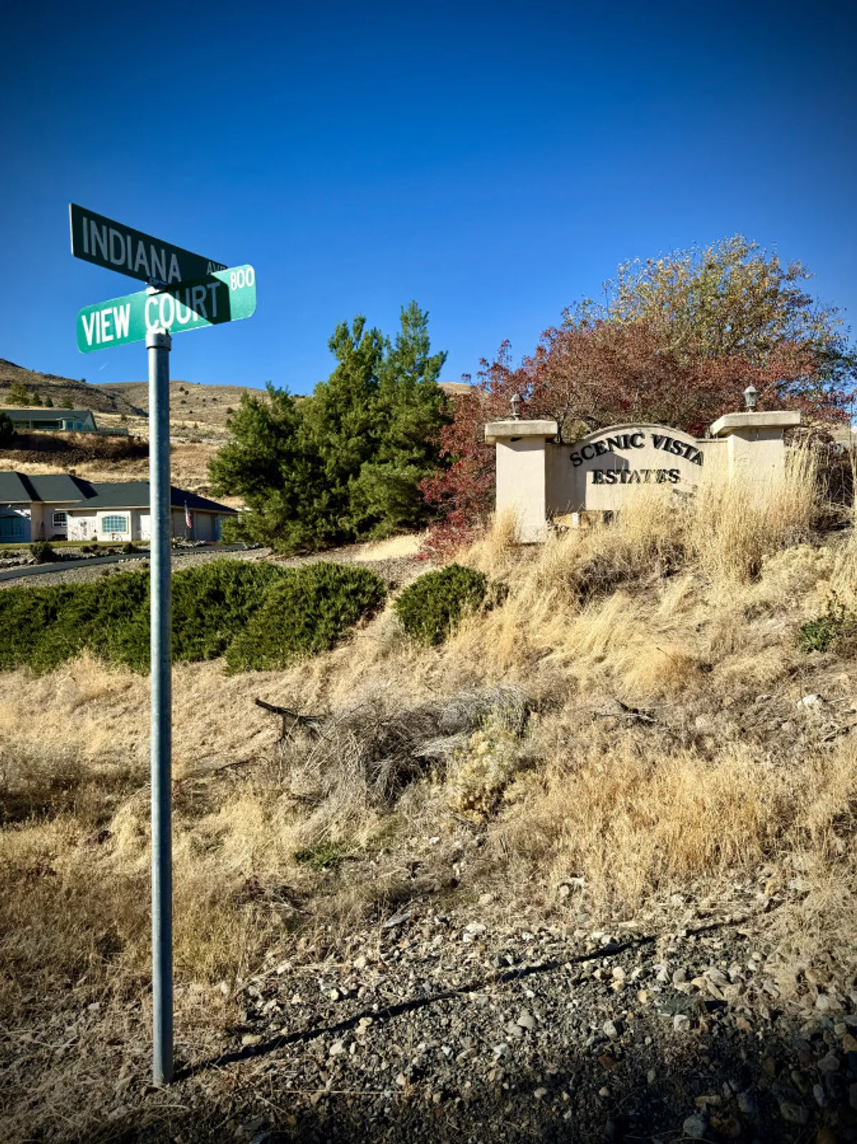 A view of the Scenic Vista Estates sign at a street corner, surrounded by natural vegetation. The image sets the scene for the neighborhood and highlights the peaceful, scenic surroundings beyond the home itself.