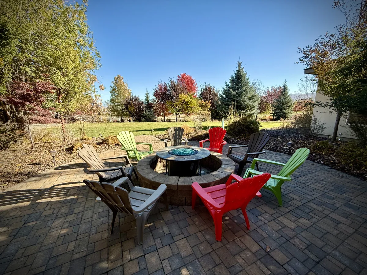 An outdoor ground-level patio centered around a fire pit, with colorful chairs arranged for communal gatherings and surrounded by trees. The setting feels lively and welcoming, perfect for socializing, roasting s'mores, or enjoying quiet evenings outdoors.