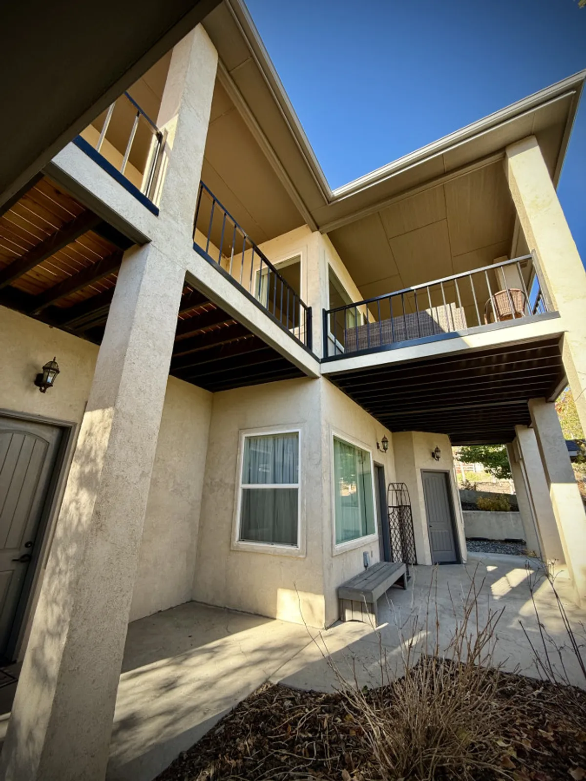 A two-story home with a welcoming balcony overlooks a landscaped area, with large windows and a spacious door offering glimpses inside. The balcony and exterior seating hint at outdoor relaxation and group gatherings, while the surrounding greenery provides a tranquil atmosphere. The structure’s elevation suggests potential views of the surroundings, possibly including the nearby golf course.